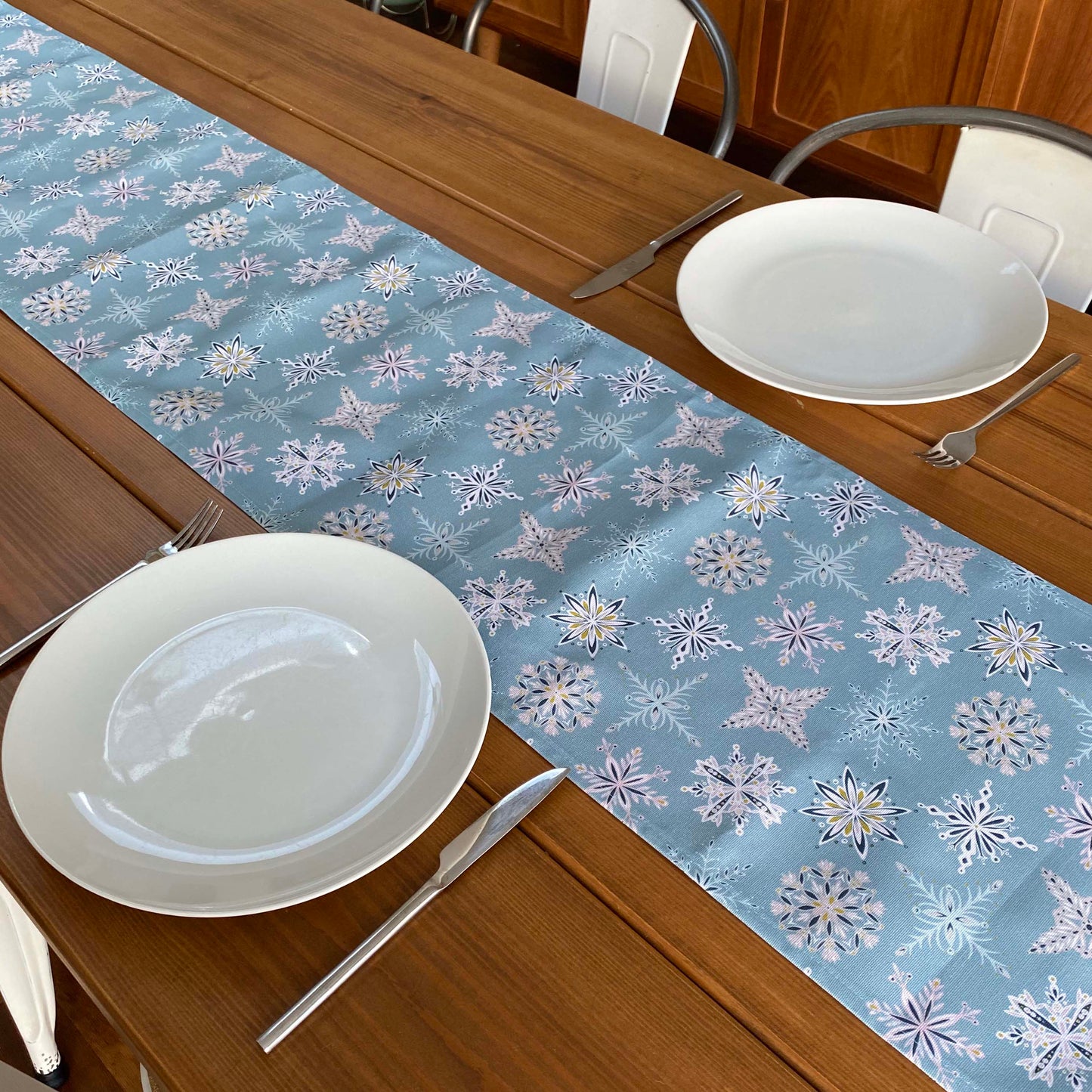 Blue Snowflake table runner has been placed down the centre of a wooden table. The table has been set for two people.