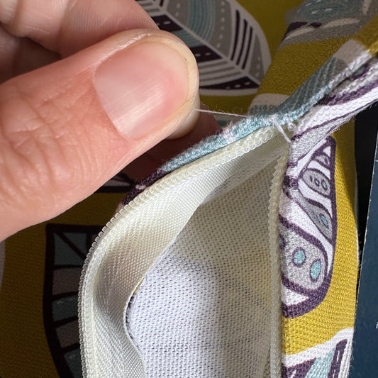 Close-up of a hand holding open a zippered pouch or case, showing the white mesh interior and patterned exterior fabric with yellow, purple, and teal leaf motifs.