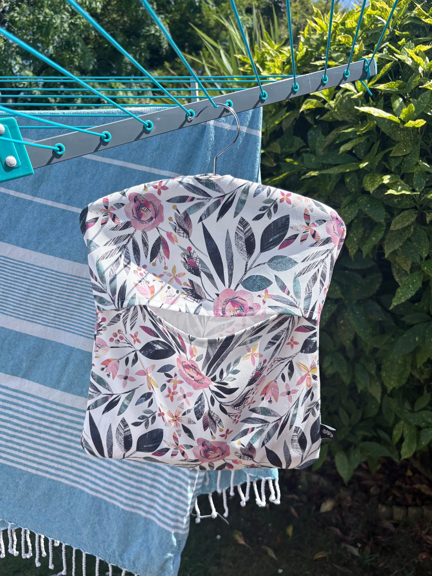 A Summer Floral patterned peg bag hanging on a clothesline with greenery in the background.