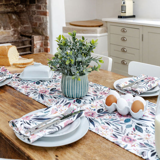 Dining table set with Summer floral table runner and matching Napkins, plates, and a vase with greenery.