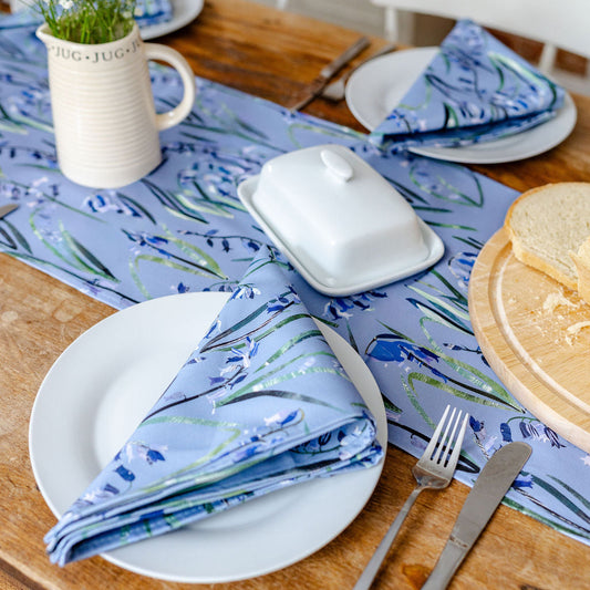 Dining table setting with bluebell floral runner and matching napkins, plates, and cutlery.