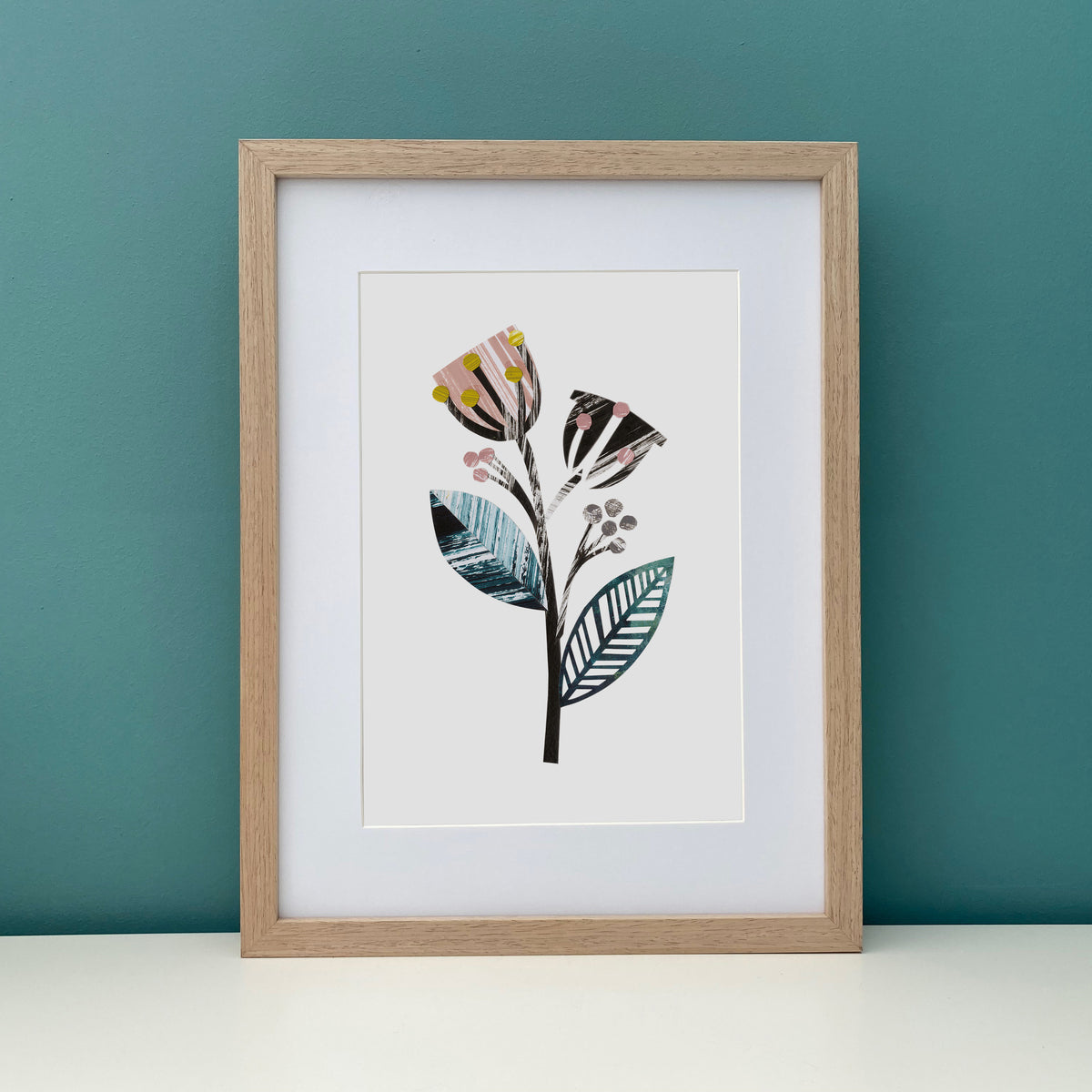 Framed artwork of a stylized floral design on a teal wall.