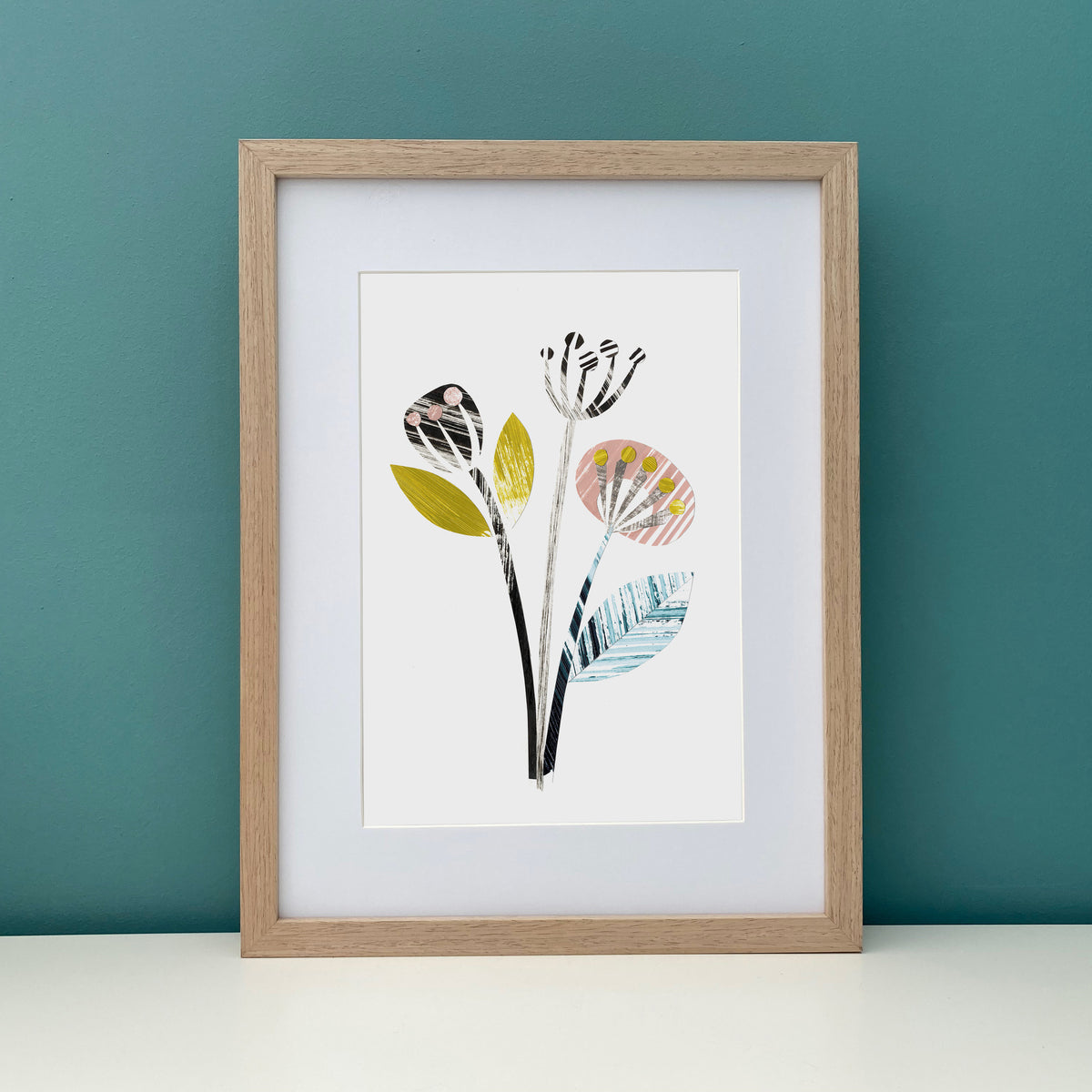 An abstract artwork of flower seed heads has been placed in a wooden from against a teal wall.