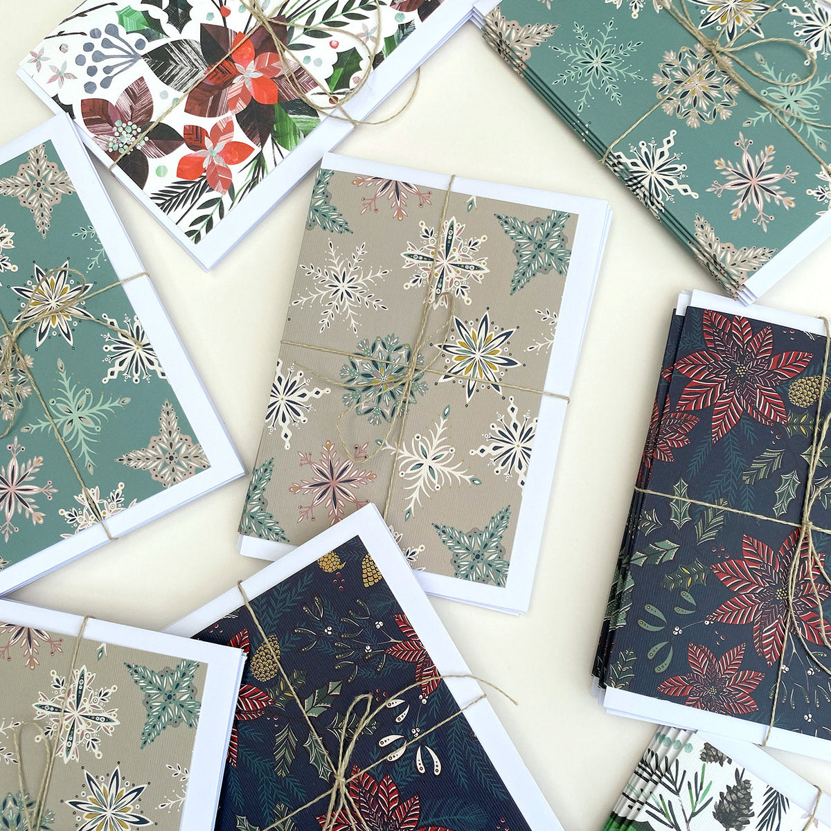A styled flat-lay of multiple greeting cards with winter botanical and snowflake patterns, wrapped in twine and arranged on a light cream background.