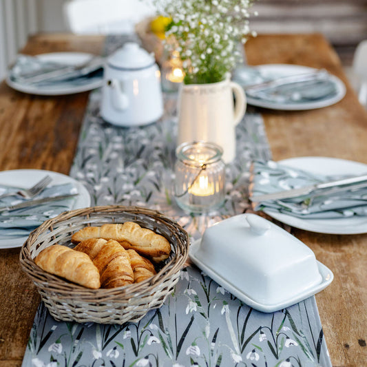 Dining table set with plates, cutlery, a basket of bread, and a pitcher on a Snowdrop Table runner