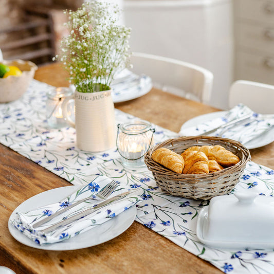 Set dining table with a basket of bread, plates, and cutlery on a Cornflower table runner.