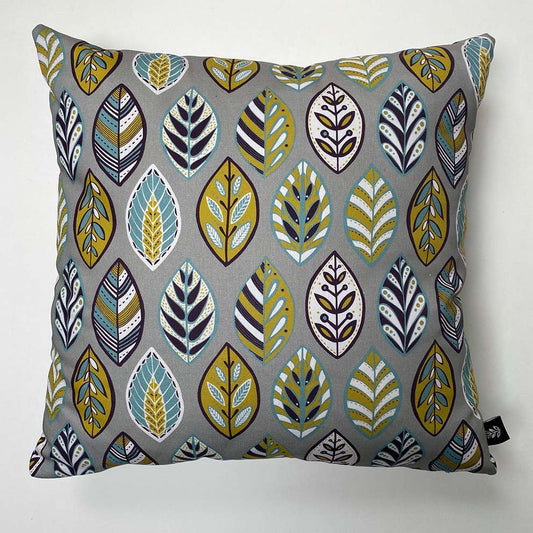 Grey Beech leaf square cushion, measures 45 x 45cm and has been placed on a plain white background.  The simple leaf motif features  Blue, white, yellow and aubergine on a mid grey background.  The pattern has a retro/skandinavian feel to it.