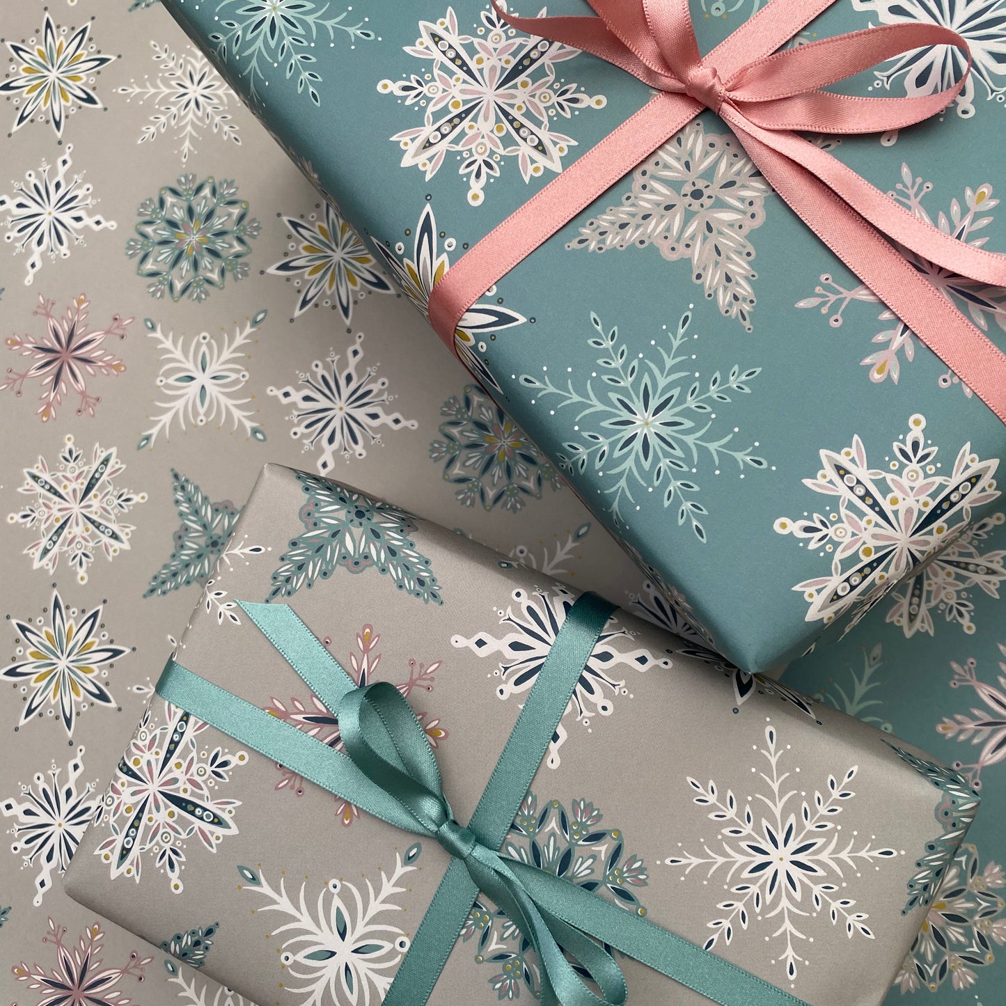 Two presents have been wrapped up in the snowflake Christmas wrapping paper.  One has been wrapped up in the Blue Snowflake Gift Wrap and the other has been wrapped in the grey snowflake Christmas Gift Wrap.