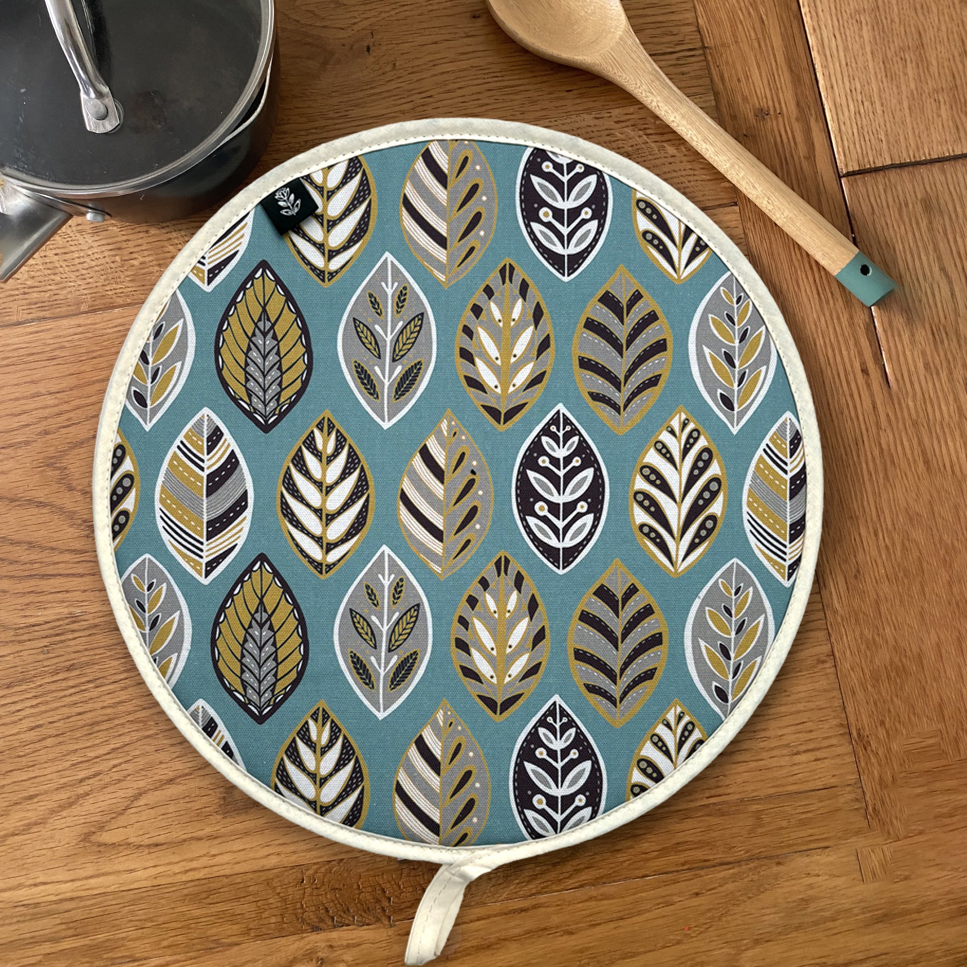 Blue Leaf Aga Cover has been placed on a wooden table with a saucepan and a wooden spoon.