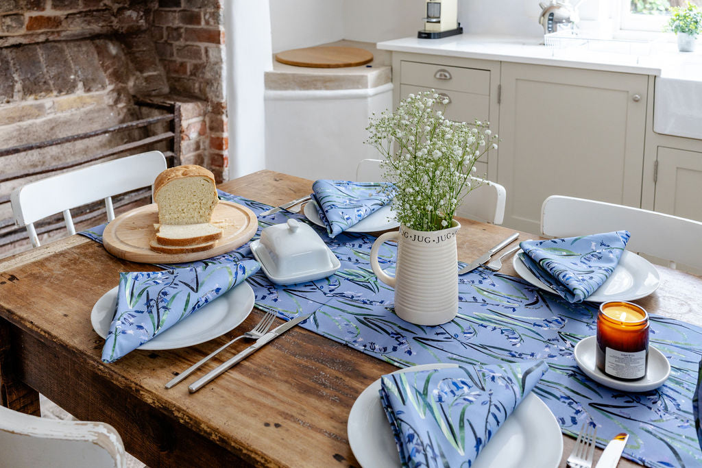 Dining table set with plates, cutlery, and a vase on a blue patterned tablecloth in a kitchen.