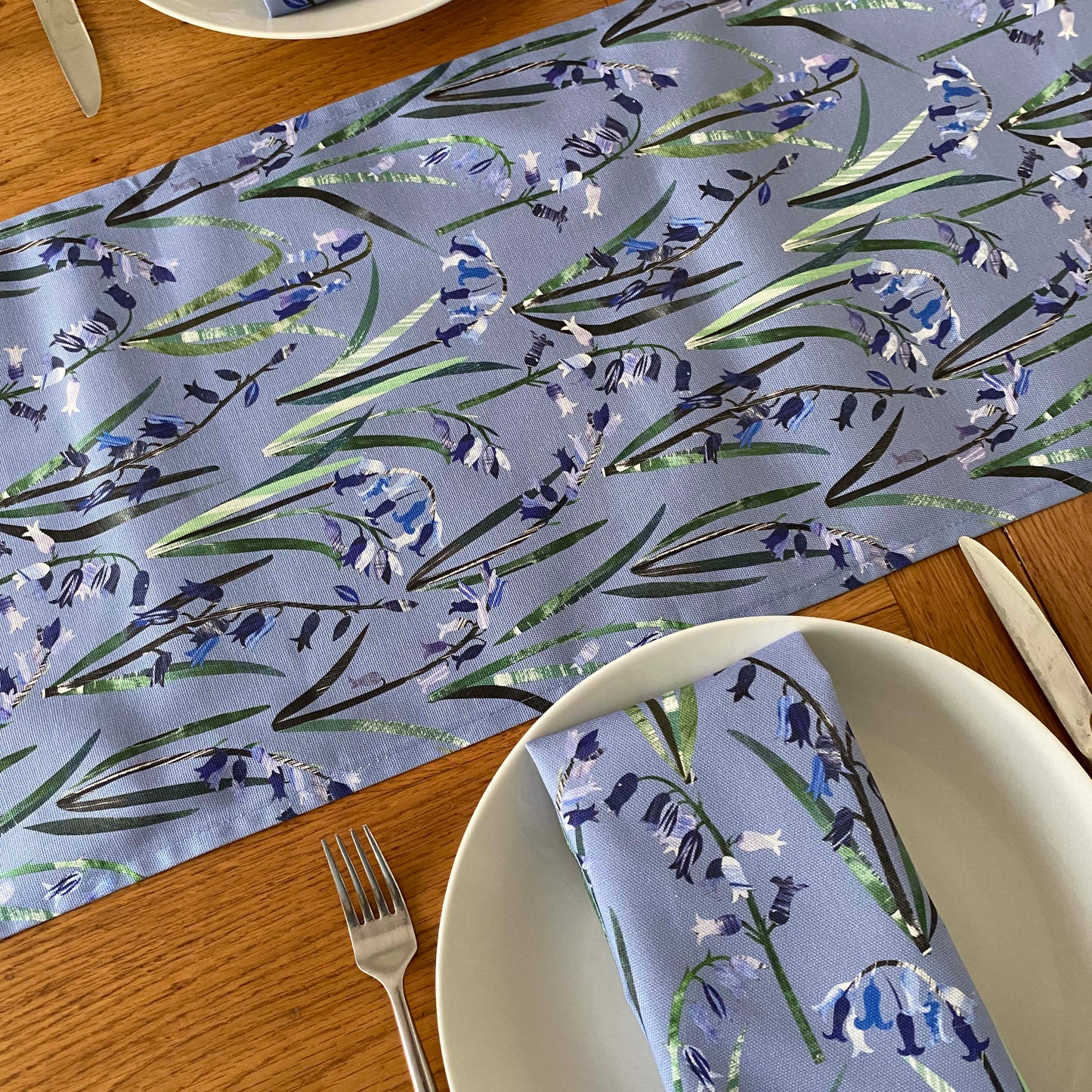 Table setting with a bluebell floral-patterned table runner  and napkin on a wooden table.
