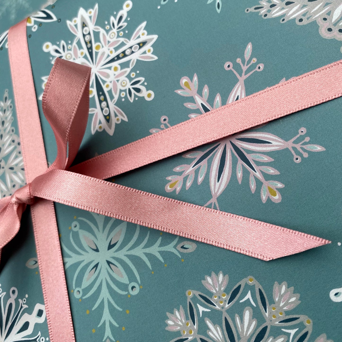 A close up of a present that has been wrapped in the blue Snowflake gift wrap and has been tied with coordinating dusky pink satin ribbon in a bow.