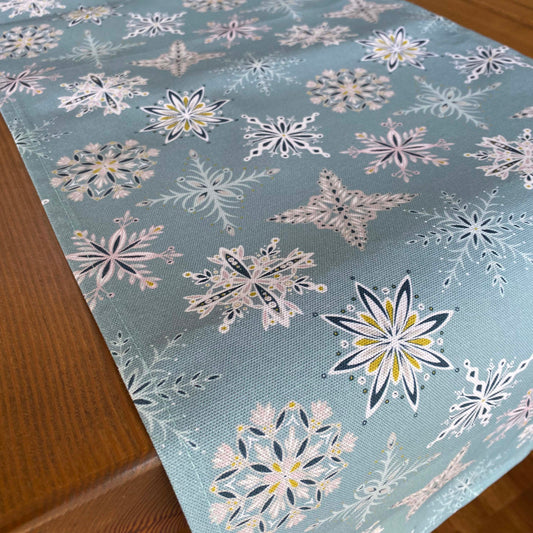 Close up of the Blue Snowflake table runner.  The table runner features different snowflake motifs in white, dark blue, grey, dusky pink and yellow.