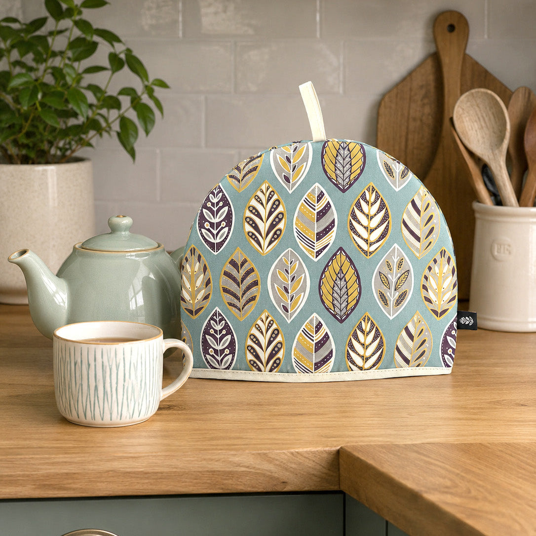  Blue Leaf Tea Cosy has been placed on a wooden worktop in a kitchen with a Tea Pot and a cup of tea.