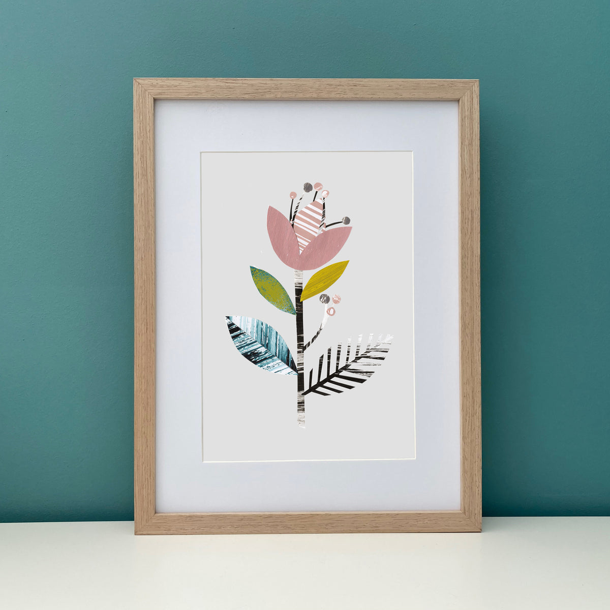 Framed artwork with a colorful floral design on a teal wall.
