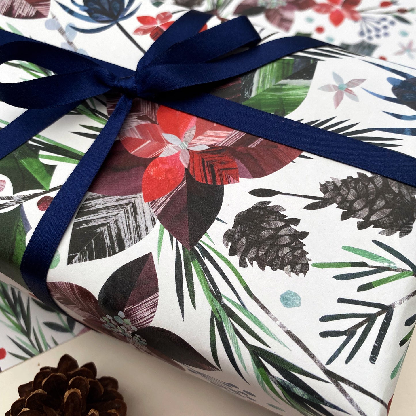 A close up of a present that has been wrapped in the winter Floral Christmas wrapping paper and has been tied with dark blue satin ribbon in a bow.The present has been placed on a sheet of the winter floral gift wrap.