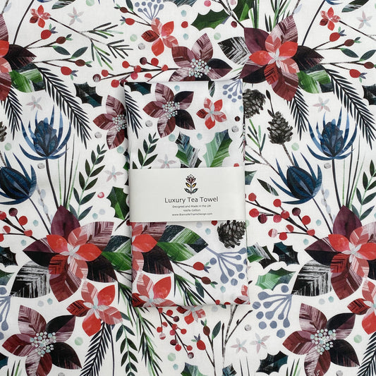 A winter Floral Tea Towel has been packaged in a branded belly band and has been placed on an opened out tea towel featuring the same design.