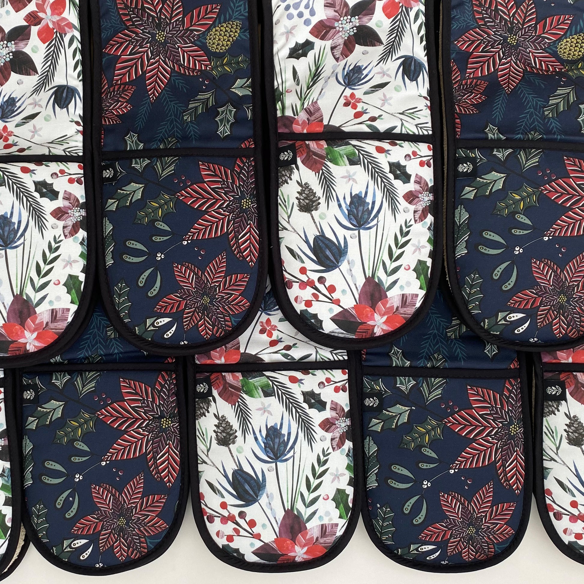 Christmas Oven Gloves placed side by side and overlapping in the navy Poinsettia and Winer Floral Pattern.