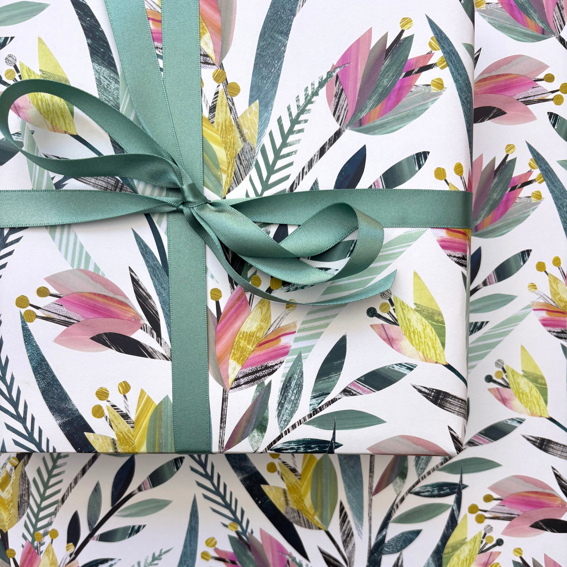 A present wrapped in the colourful tulips wrapping paper and tied with matching green ribbon in a bow.  It has been placed on a sheet of tulips gift wrap featuring the same design.