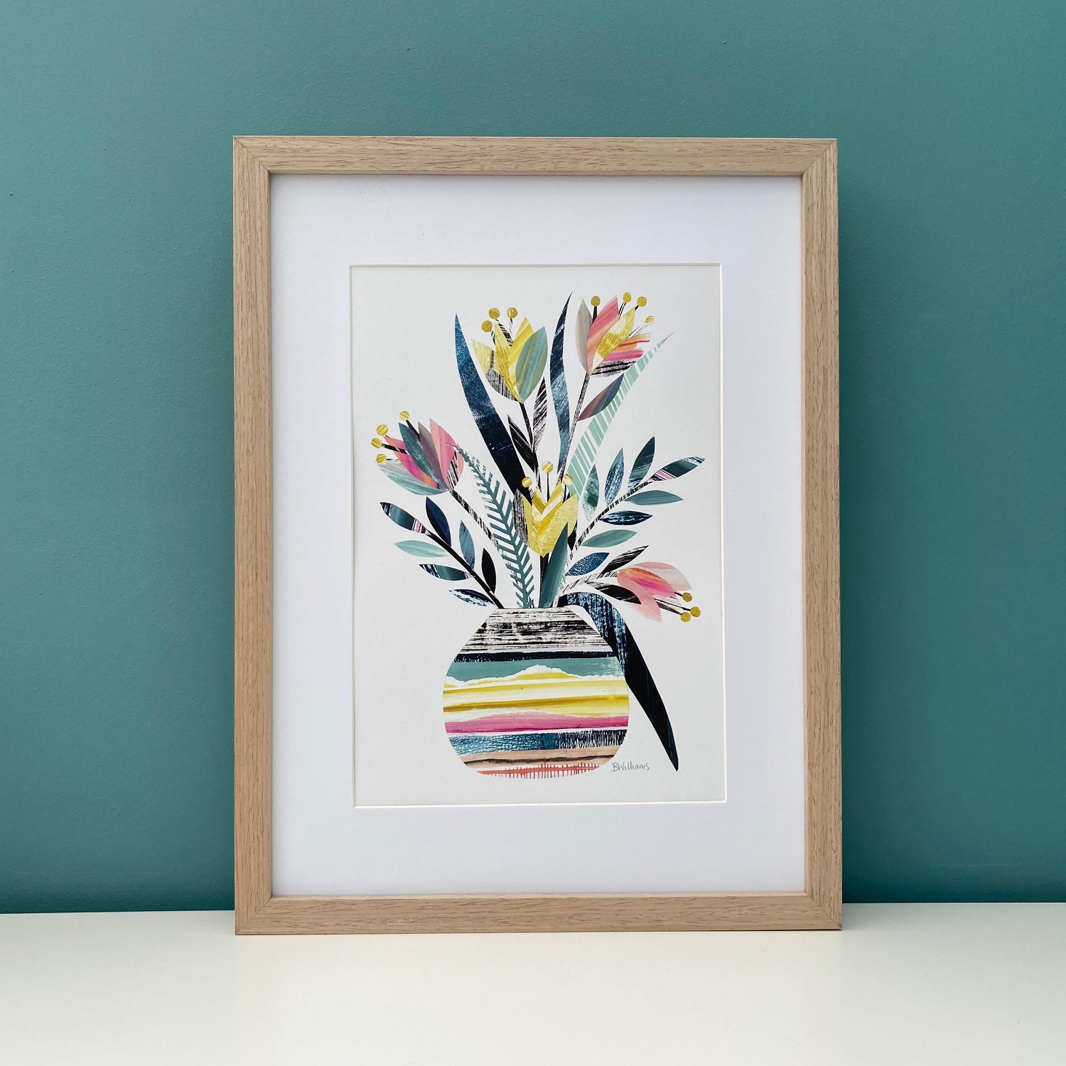 A4 Colourful Tulip Vase print is being displayed in a wooden frame with a white mount.  The Framed picture has been placed on a white shelf with a blue green wall being it.