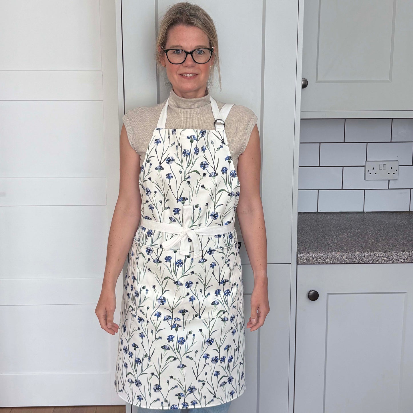 Woman wearing a blue cornflower apron in a pale grey kitchen.