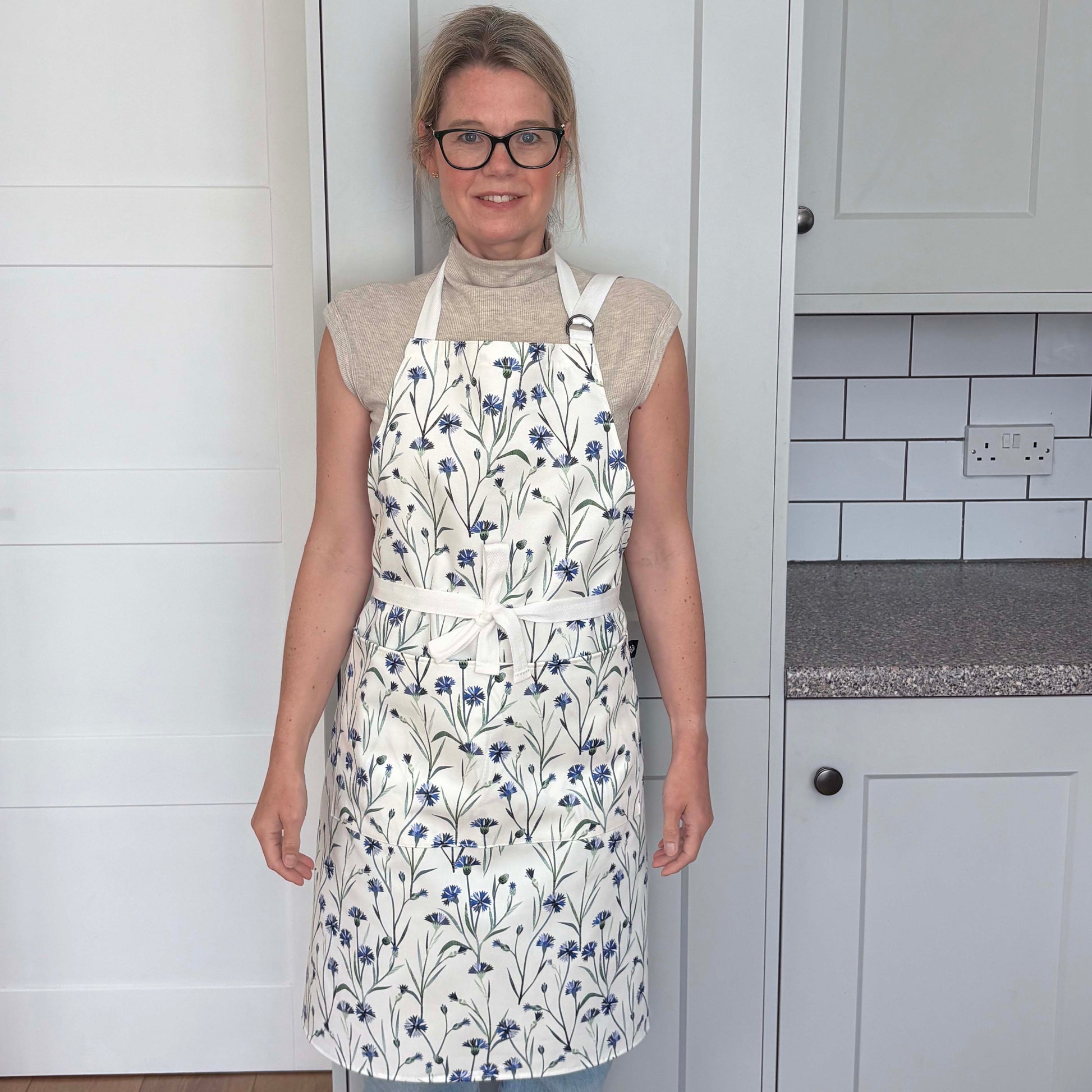 Woman wearing a blue cornflower apron in a pale grey kitchen.