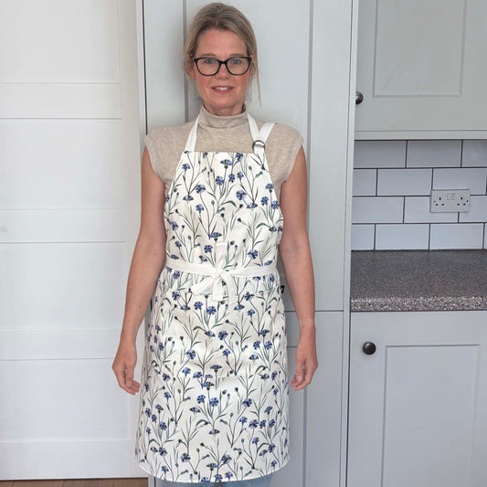 Woman wearing a blue cornflower apron in a pale grey kitchen.