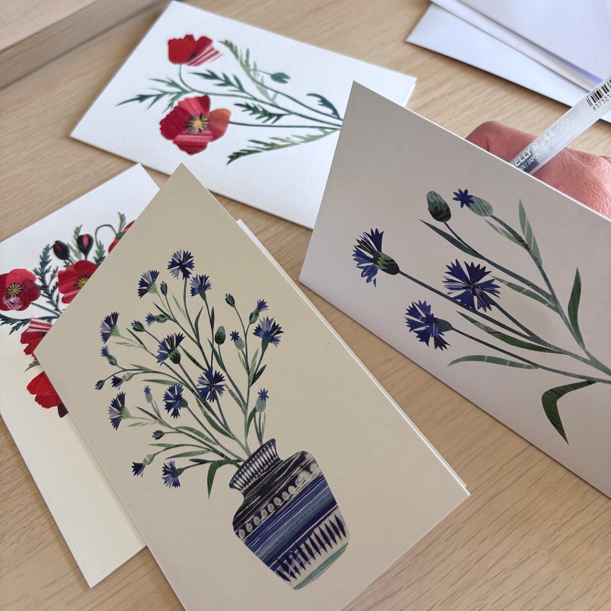 Set of Cornflower and Poppy greeting cards with floral designs on a wooden surface.