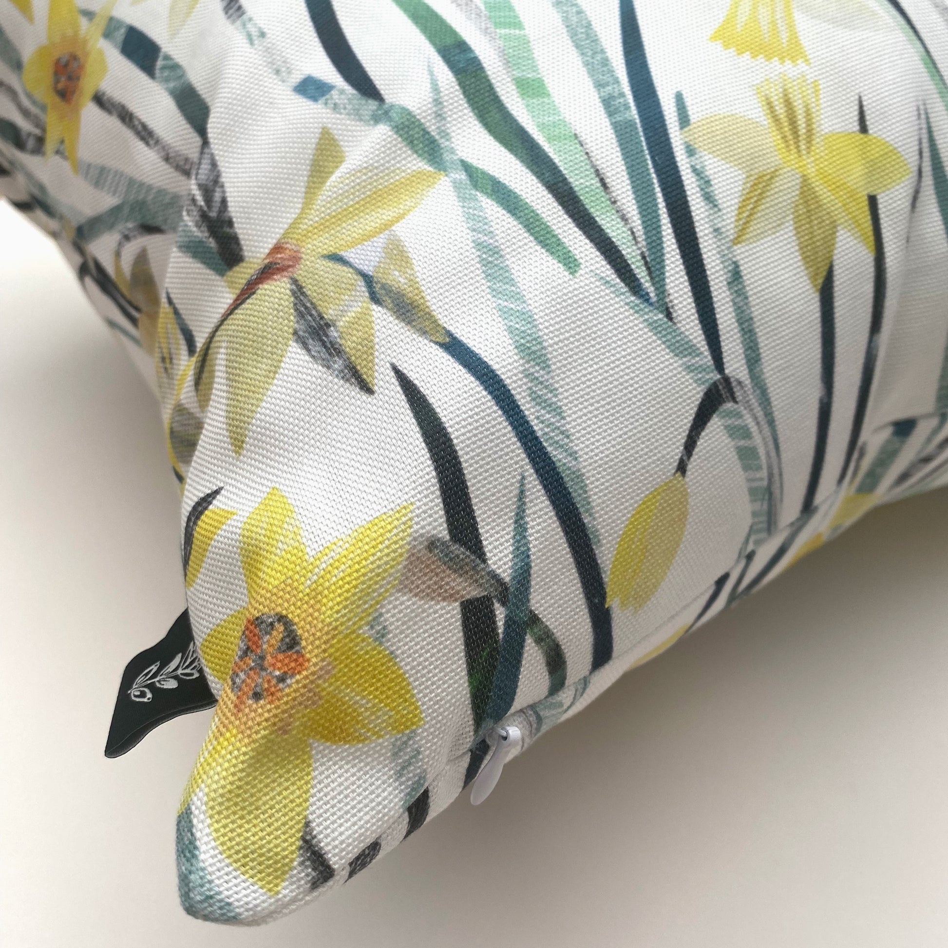 A close up of a corner of a Daffodil Cushion, it shows the concealed zip and Brand label down into the edges.  The cushion is on a white background.