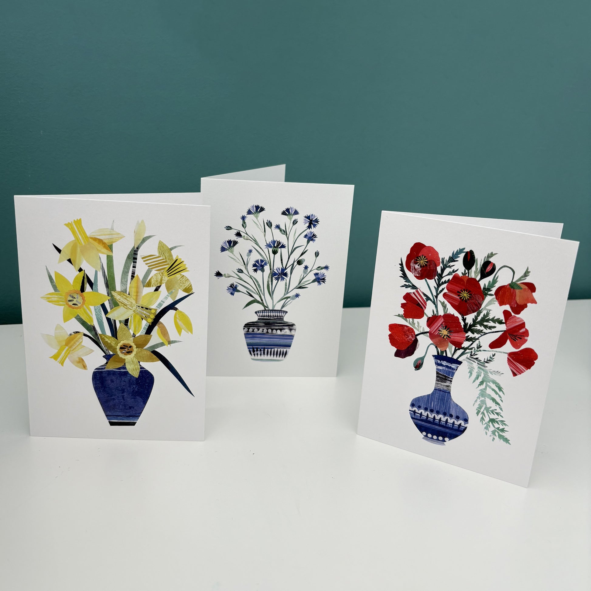 Three floral greeting cards with different flower arrangements on a white surface and teal background.