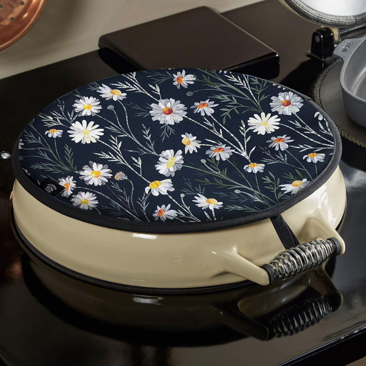 A white and Navy Daisy Aga cover has been placed on a black and cream Aga.  it is secured to the Aga using a hook.