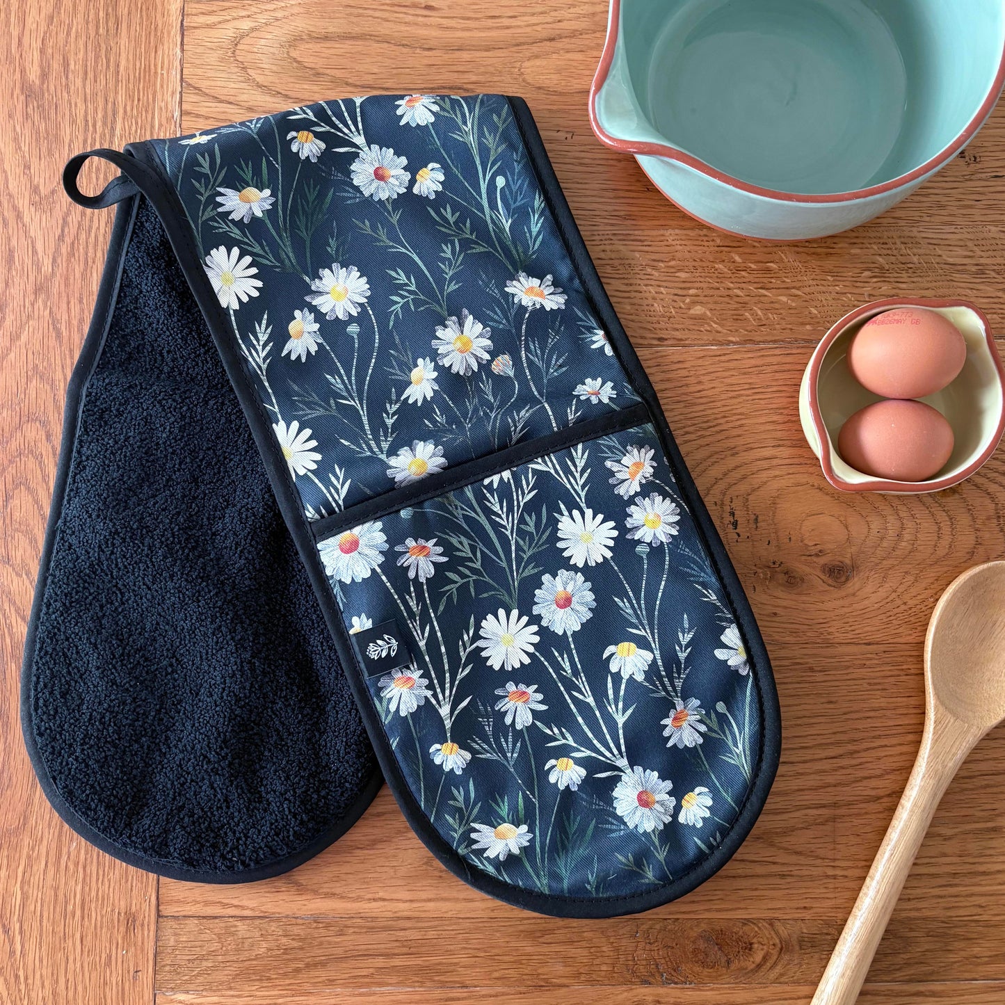 Daisy Double oven mitt on a wooden surface with a bowl, eggs, and spoon.