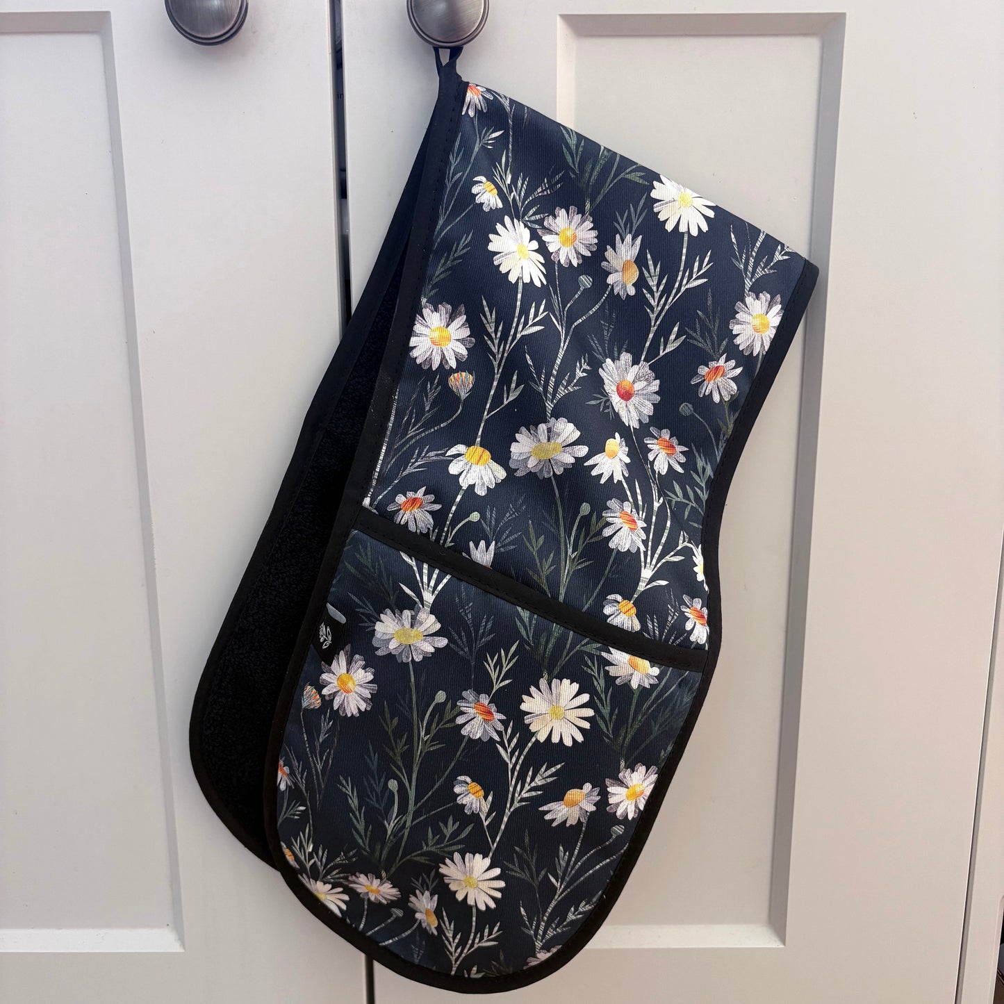 Daisy Floral-patterned oven mitt hanging on a cabinet door.