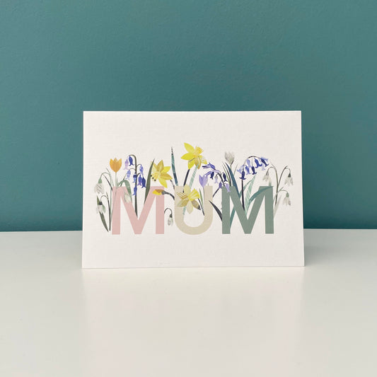 Floral Mum card has been stood on a white shelf with a blue green background.