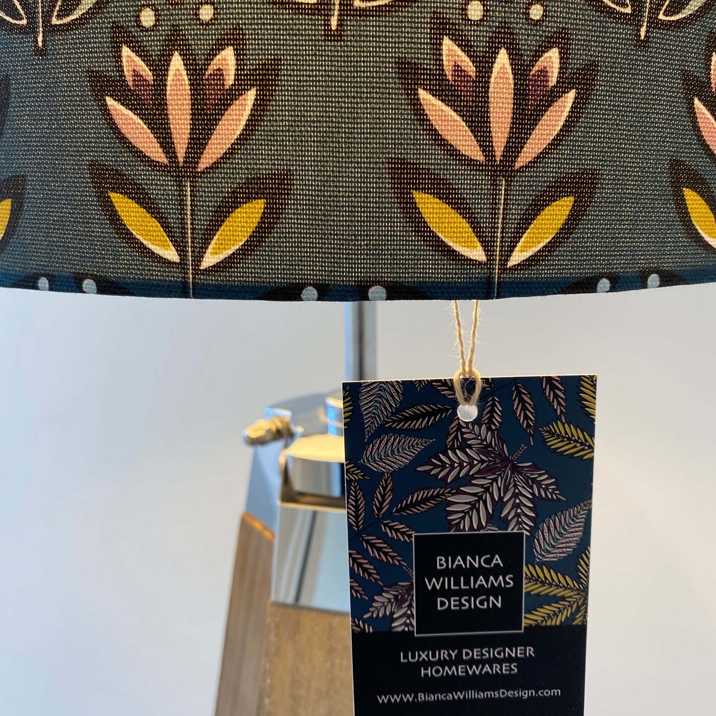 close up of the Teal Flower lampshade showing how the light glows through the lampshade and the texture of the fabric.  A swing tag can also be seen in the photograph.