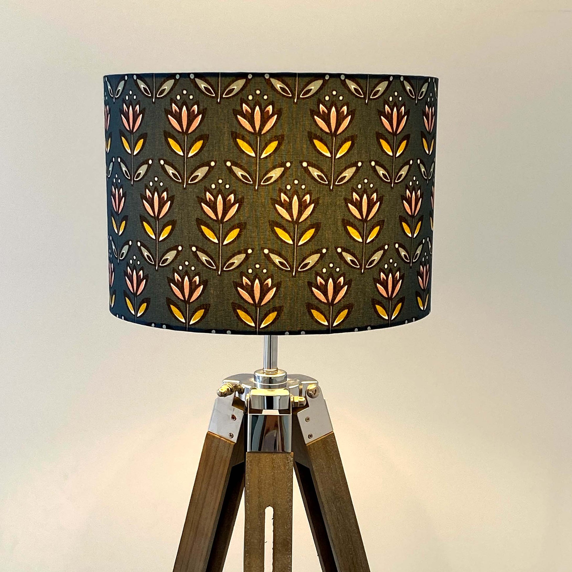 Medium Teal Flower Lampshade displayed here on a wooden tripod floor lamp.  The design features a simplified flower motif in black, white, yellow, blue, dusky pink and aubergine on a Teal background.  The light is shown on in this photograph.