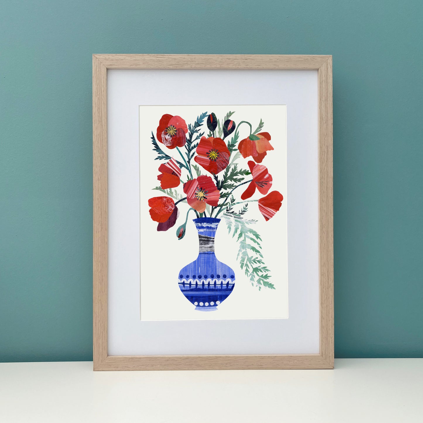 Framed artwork of red poppy flowers in a blue vase on an off white background has been placed against a teal wall.