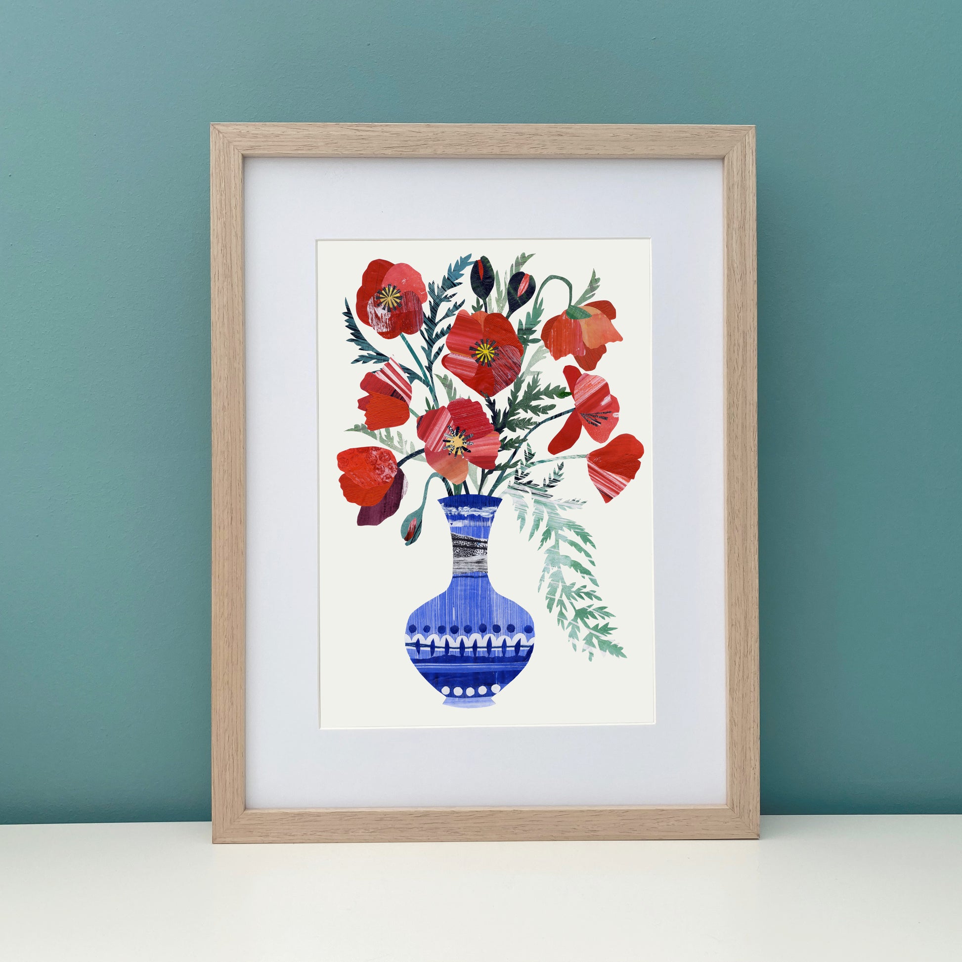 Framed artwork of red poppy flowers in a blue vase on an off white background has been placed against a teal wall.