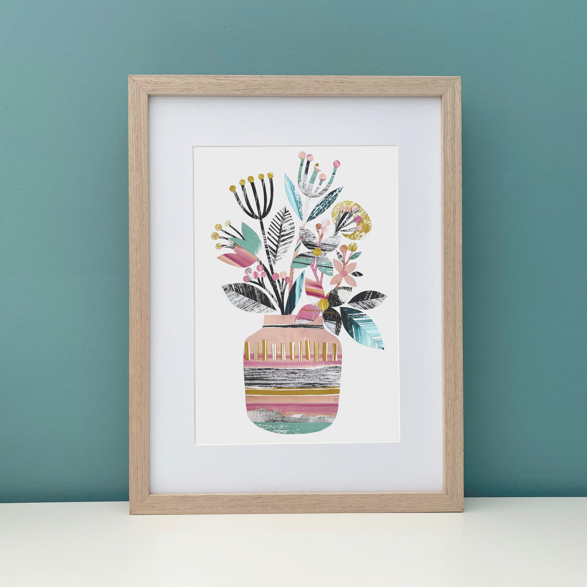 Framed artwork of a colorful vase with floral design on a teal wall.