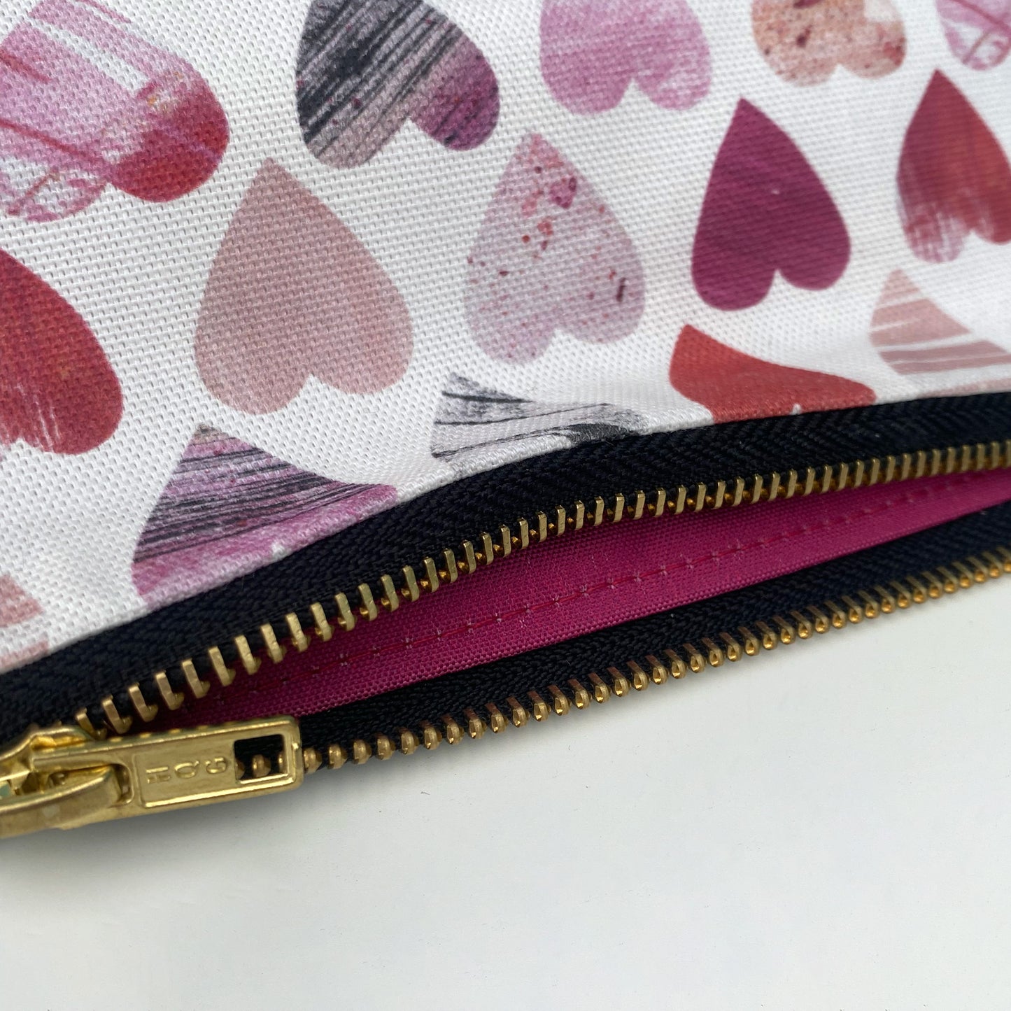 Close up of a small Hearts wash bag showing the textured printed hearts pattern, gold metal zip and bright pink lining.