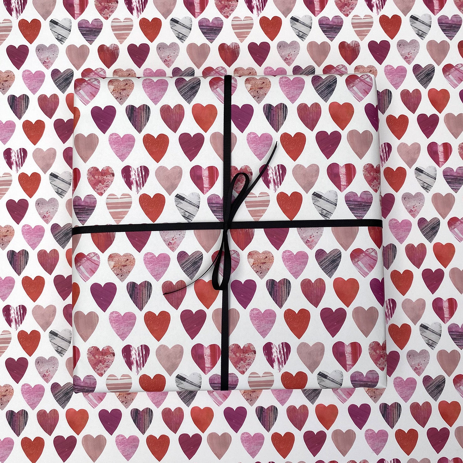 A present wrapped in hearts gift wrap has been paced onto of a sheet of matching hearts wrapping paper.