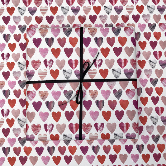A present wrapped in hearts gift wrap has been paced onto of a sheet of matching hearts wrapping paper.