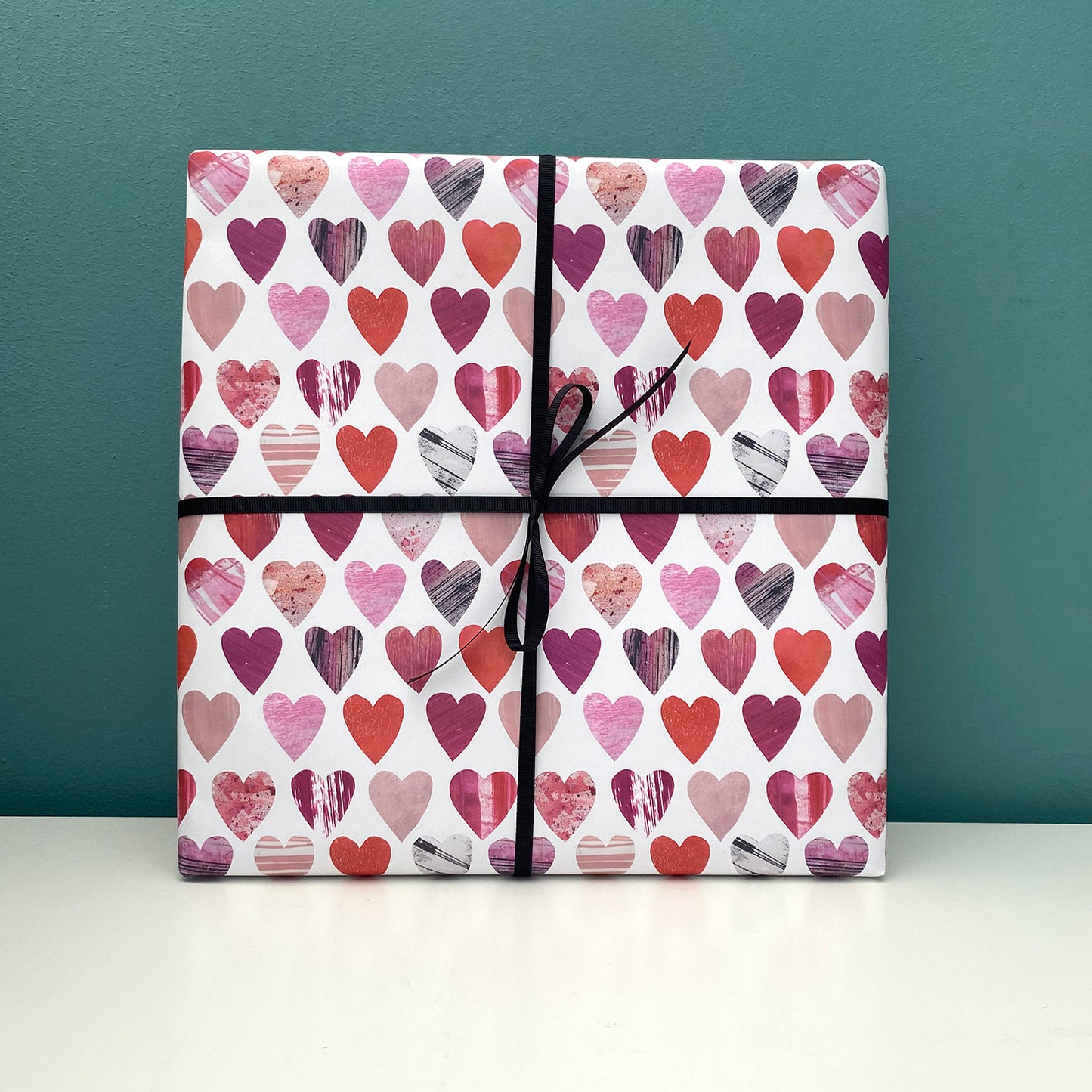 A present wrapped in the hearts gift wrap has been placed on a white shelf agains a blue green wall.