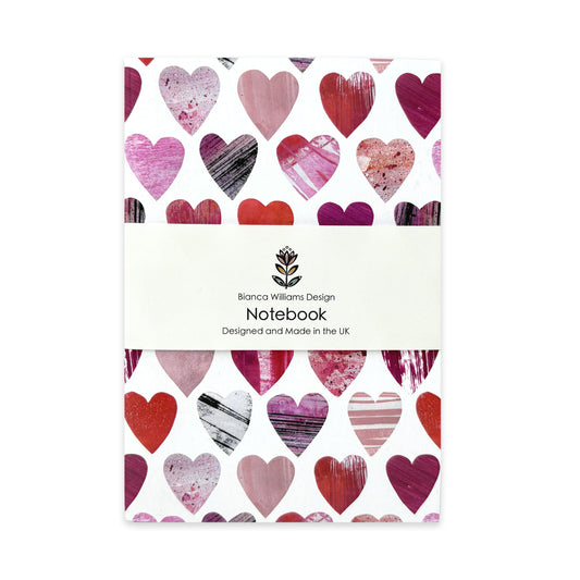 A little notebook featuring textured pink and red hearts has been packaged in a branded belly band and placed on a white background.
