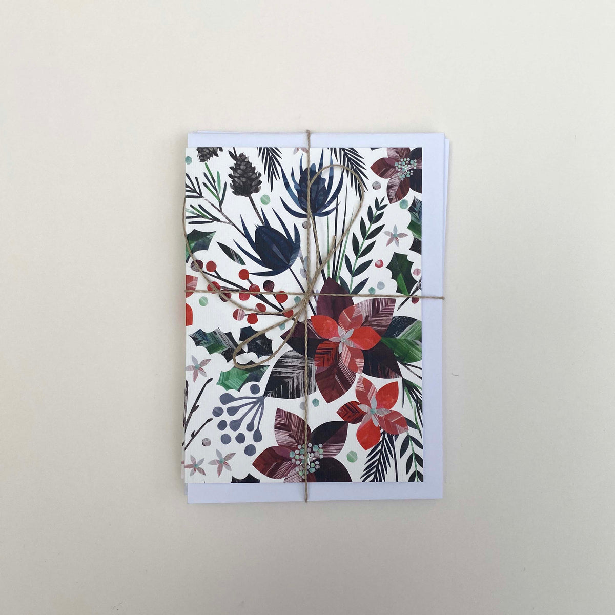 A pack of 5 winter floral christmas cards and envelopes have been tied with brown twine and placed on a white background.