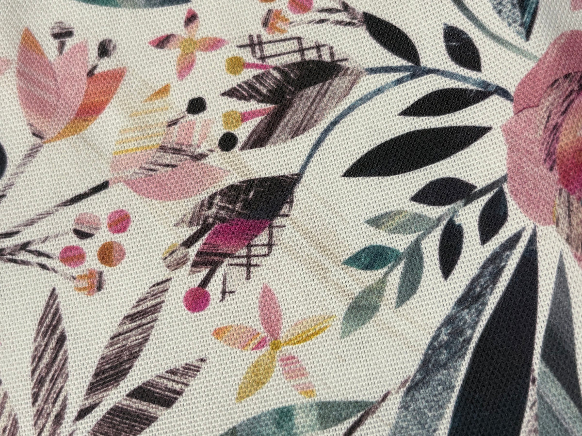 A close-up of a woven fabric with a botanical pattern featuring pink flowers, green and teal leaves, and dark charcoal accents on a cream background.