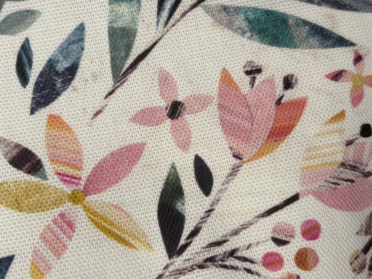 A close-up of a woven fabric featuring a botanical pattern with pink, yellow, and teal leaves and flowers on a cream background.