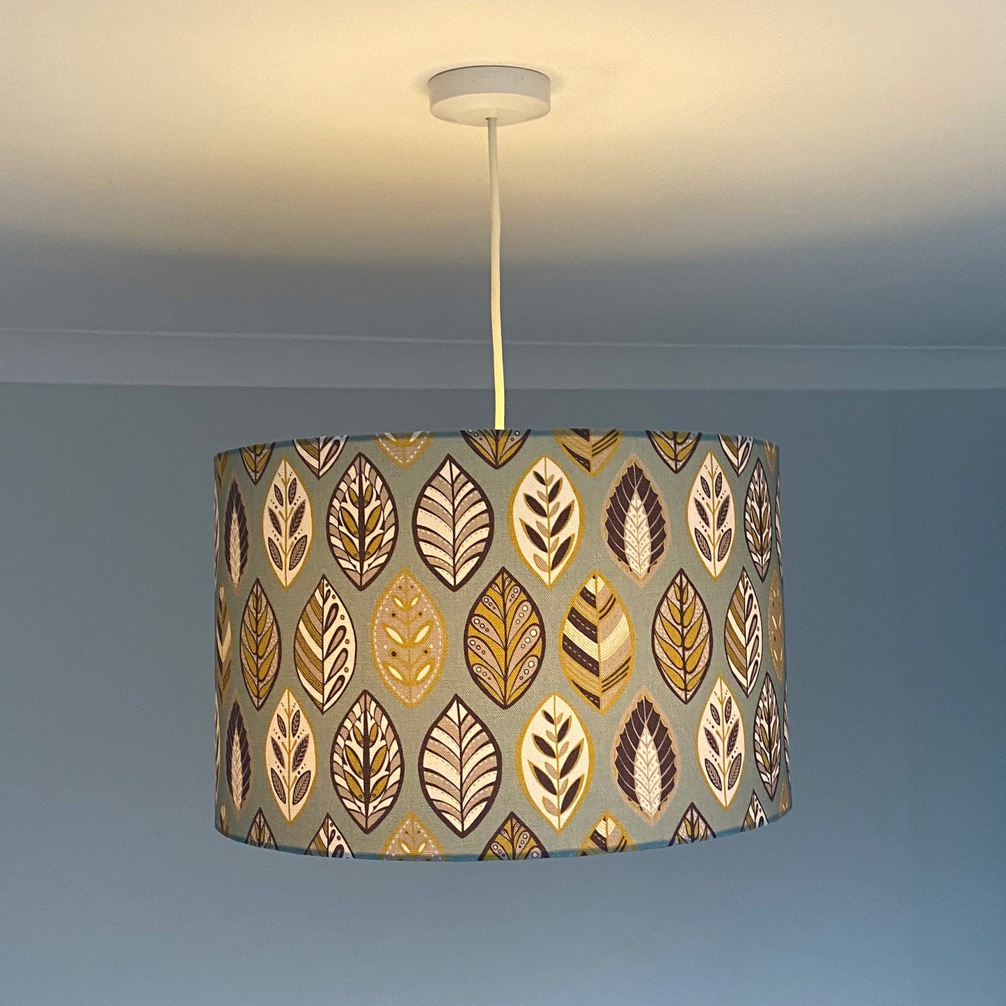 Large Blue Beech leaf Lampshade, shown here on a ceiling pendant. The pattern features a Skandi style Blue, yellow, grey and white Leaf pattern on a Blue Background.  The light is shown on in this photograph.
