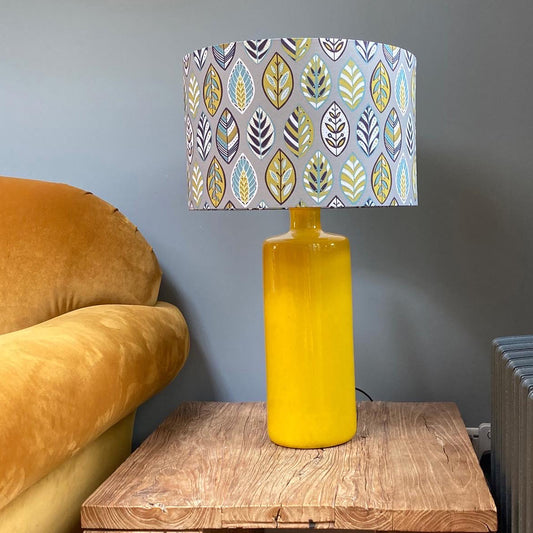 Large Grey Beech Leaf Lampshade shown here on a large yellow ceramic table lamp.  Which has been placed on an rustic oak coffee table against a grey back wall.