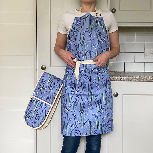 Model wears a Light Blue Bluebell apron with her hand placed in the the two front pockets.  The Apron also has an adjustable neck strap.